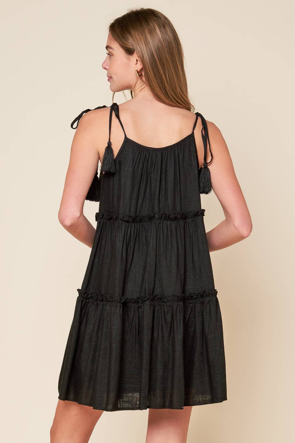 A black solid woven mini dress featuring U neckline, shoulder tie with tassel, seashell trim and tiered body.