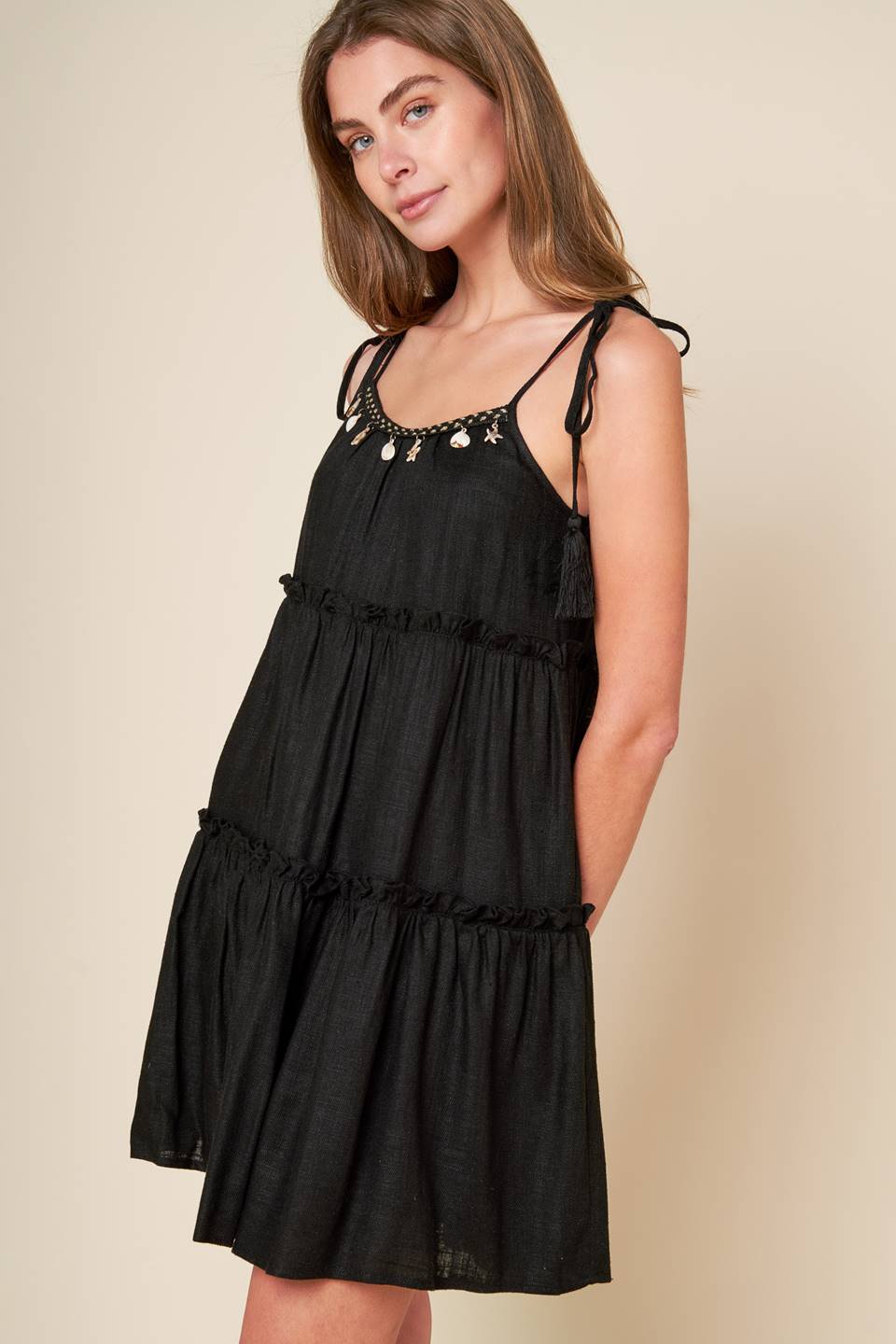 A black solid woven mini dress featuring U neckline, shoulder tie with tassel, seashell trim and tiered body.