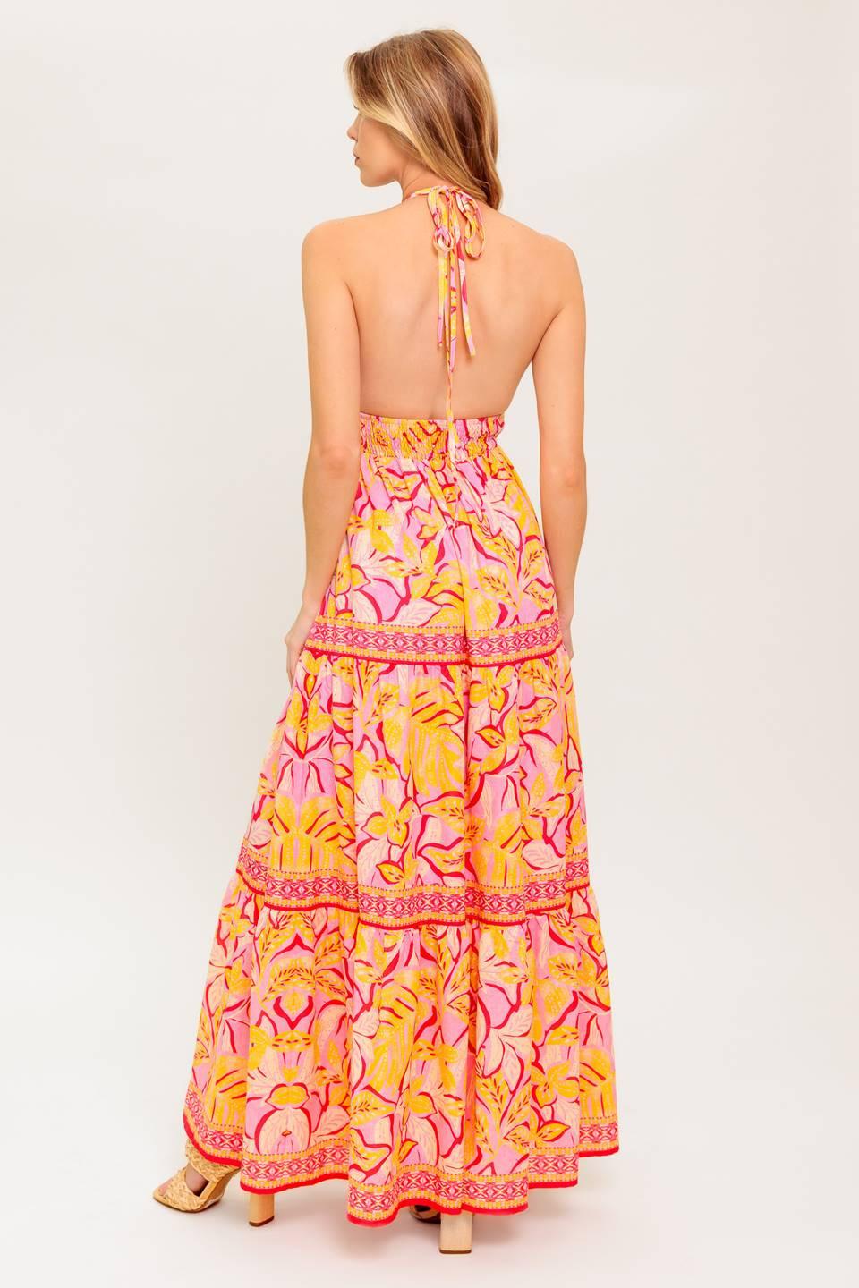 A printed woven maxi dress featuring cami top with halter tie, smocked waist yoke, tiered skirt and bare back