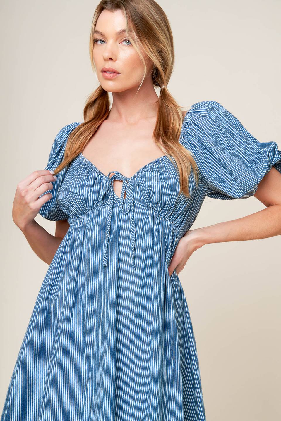 A striped blue woven mini dress featuring sweetheart neckline with front tie, short puff sleeve and elasticized empire.