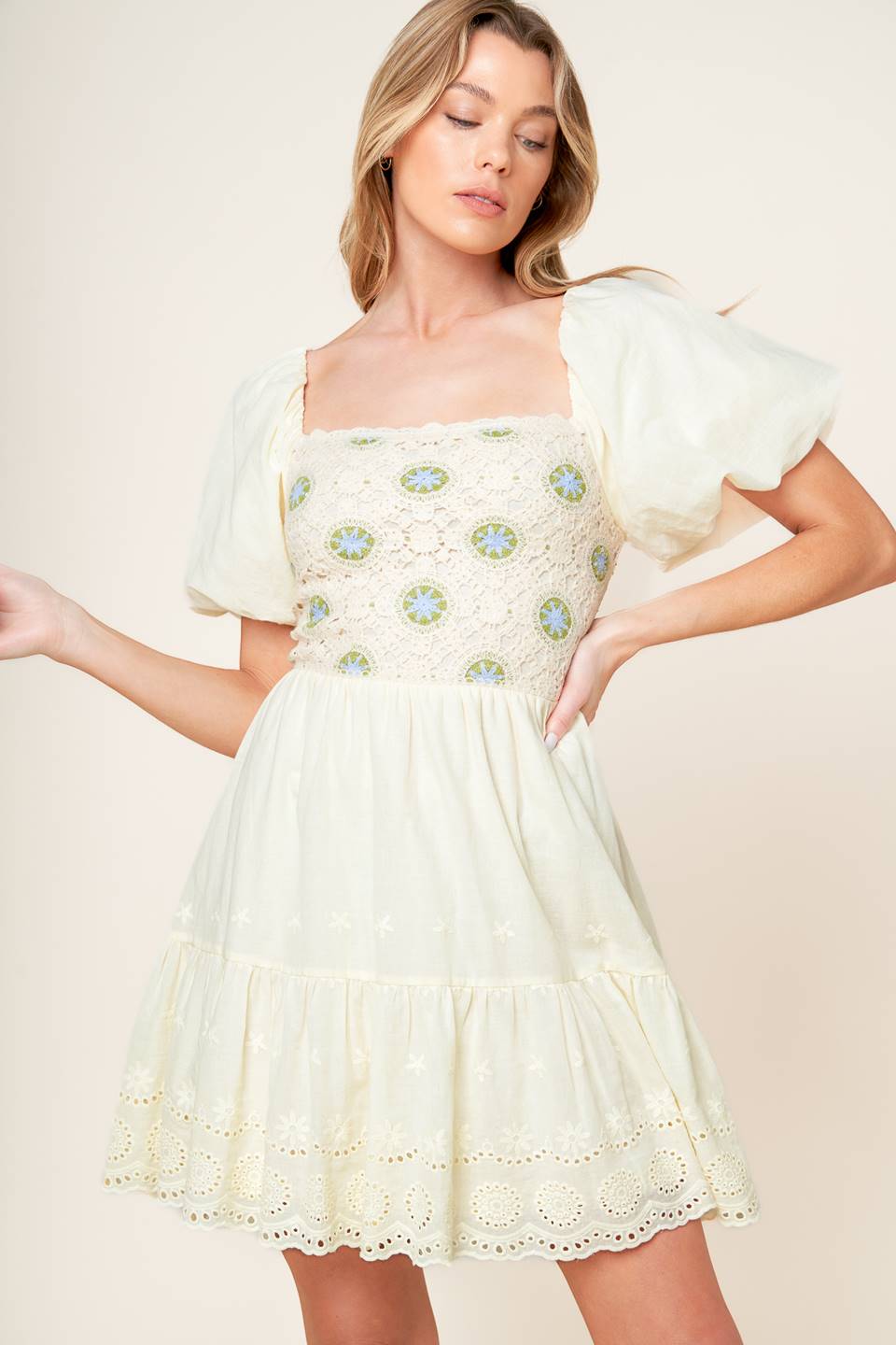 A solid woven mini dress featuring square neckline, crochet front bodice, short puff sleeve, eyelet ruffed hemline and smocked back bodice.