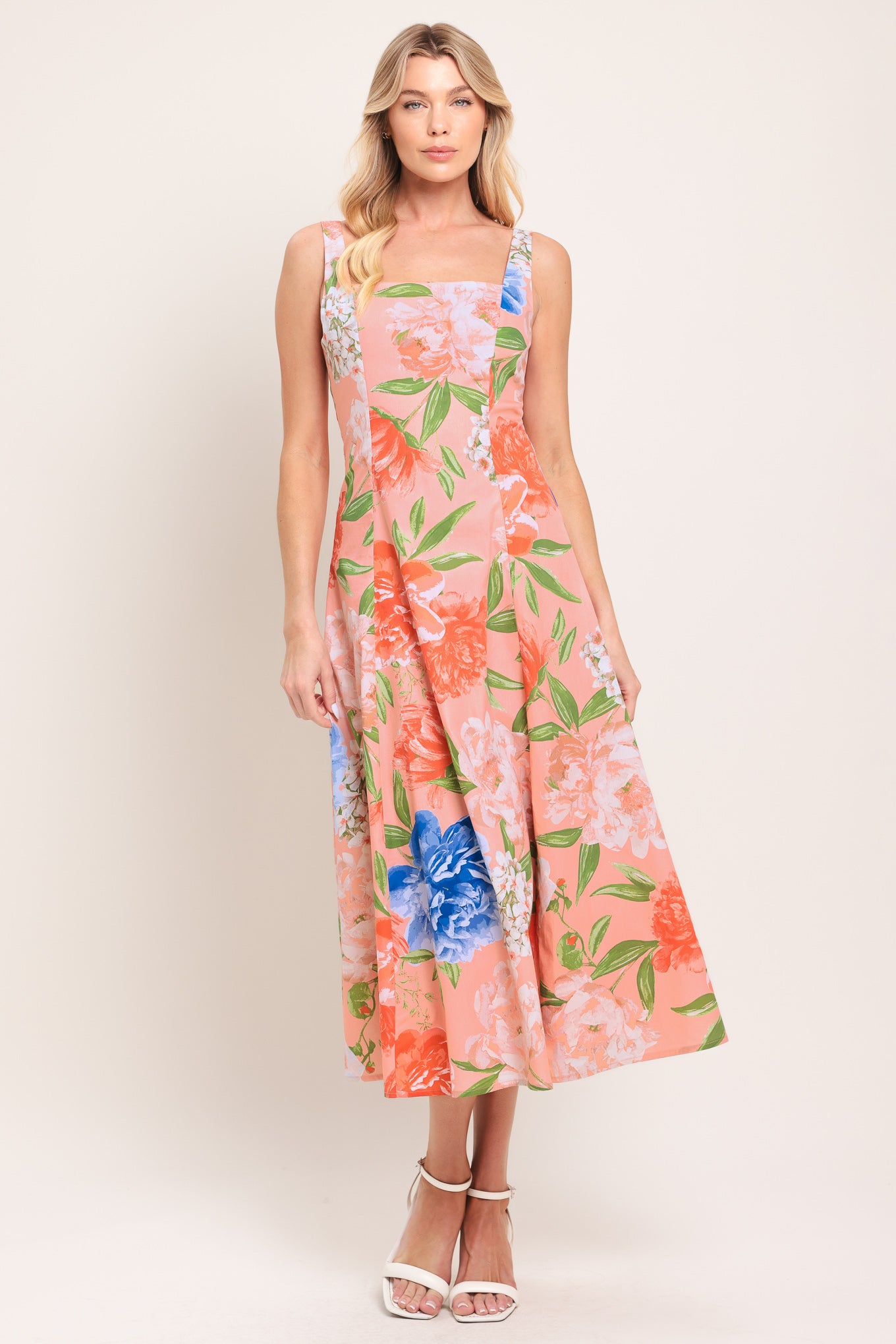 Woman wearing a sleeveless peach with pink, coral, and blue florals midi dress featuring square neckline, circle skirt and back zipper closure | Flying Tomato