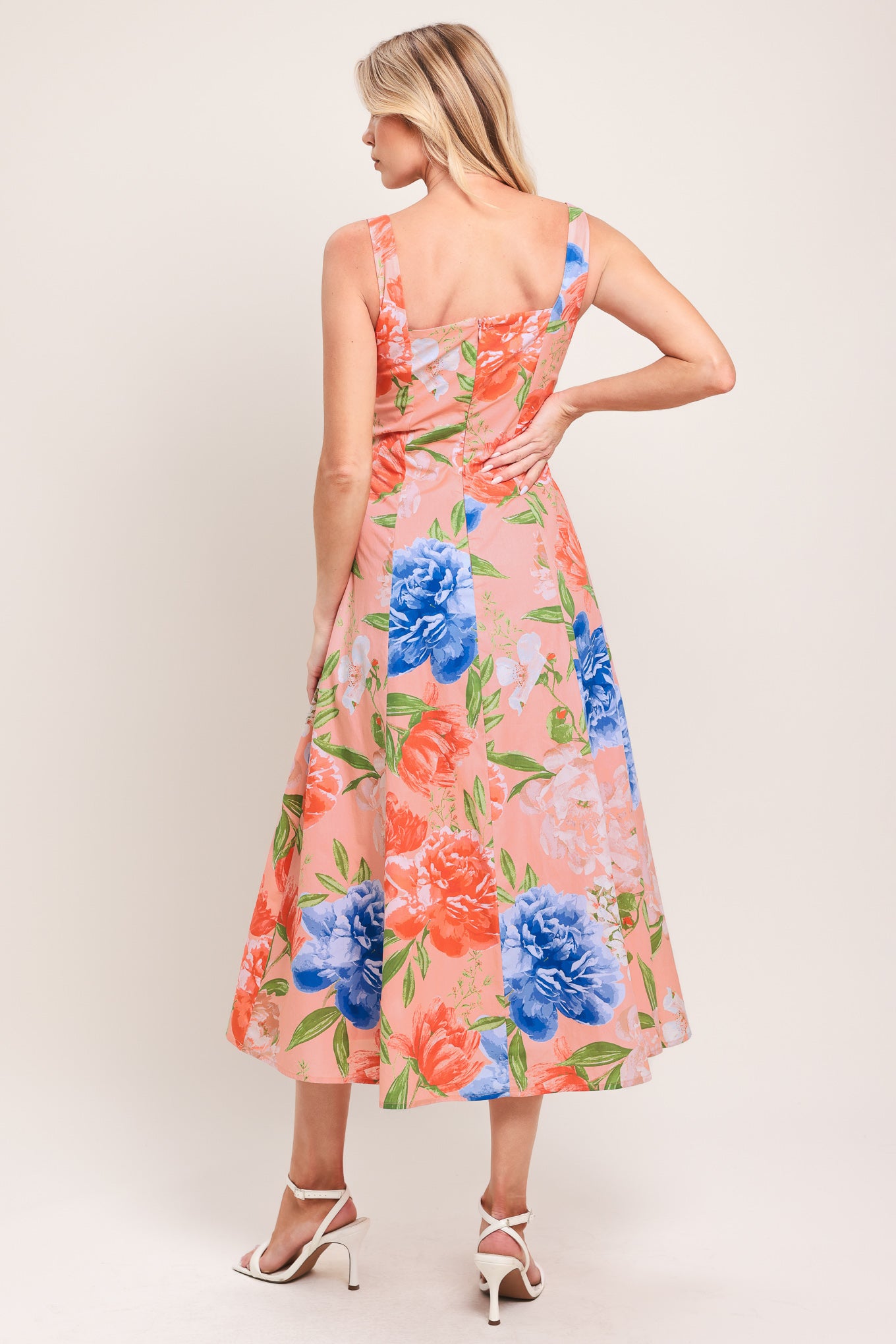 Woman wearing a sleeveless peach with pink, coral, and blue florals midi dress featuring square neckline, circle skirt and back zipper closure | Flying Tomato