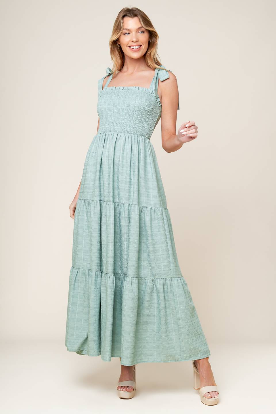 A textured solid woven maxi dress featuring straight neckline with ruffled edge, shoulder tie, smocked bodice and tiered skirt