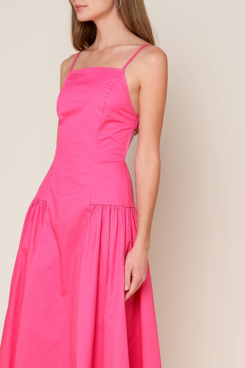 A midi dress with a solid woven fabric, sweetheart neckline, straps, and a full skirt with shirring on the sides. The back is open with a strap and zipper closure.