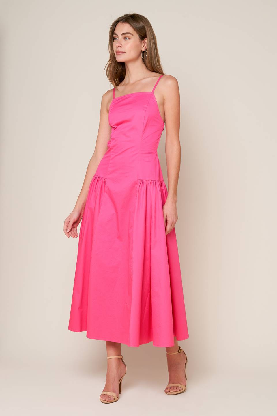 A midi dress with a solid woven fabric, sweetheart neckline, straps, and a full skirt with shirring on the sides. The back is open with a strap and zipper closure.