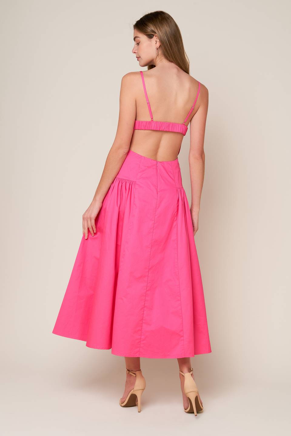 A midi dress with a solid woven fabric, sweetheart neckline, straps, and a full skirt with shirring on the sides. The back is open with a strap and zipper closure.