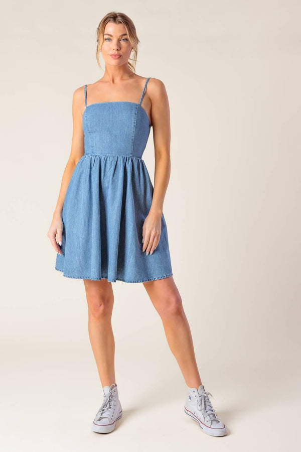 A washed denim mini dress featuring straight neckline, straps, full skirt and smocked back with cut out