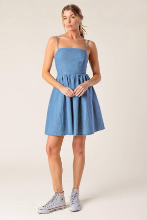 A washed denim mini dress featuring straight neckline, straps, full skirt and smocked back with cut out