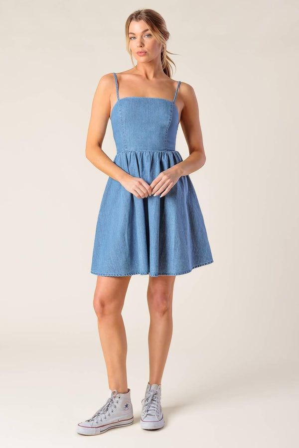 A washed denim mini dress featuring straight neckline, straps, full skirt and smocked back with cut out