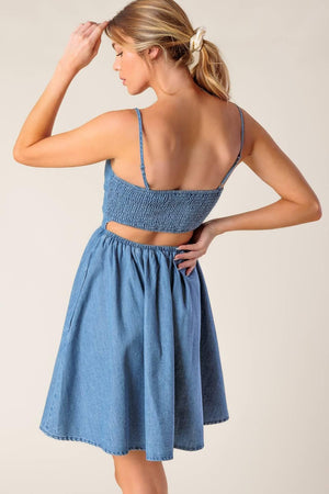A washed denim mini dress featuring straight neckline, straps, full skirt and smocked back with cut out