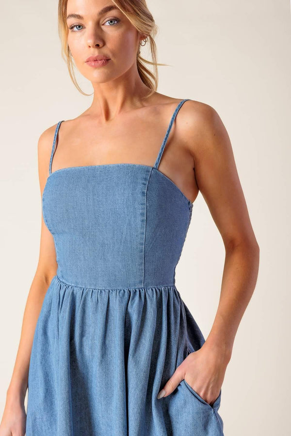 A washed denim mini dress featuring straight neckline, straps, full skirt and smocked back with cut out