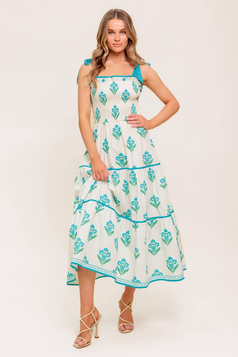 A printed woven midi dress featuring straight neckline with ruffled edge, shoulder tie, smocked bodice and tiered skirt