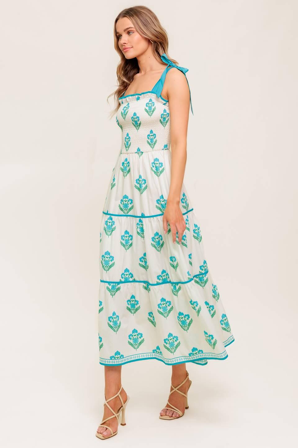 A printed woven midi dress featuring straight neckline with ruffled edge, shoulder tie, smocked bodice and tiered skirt