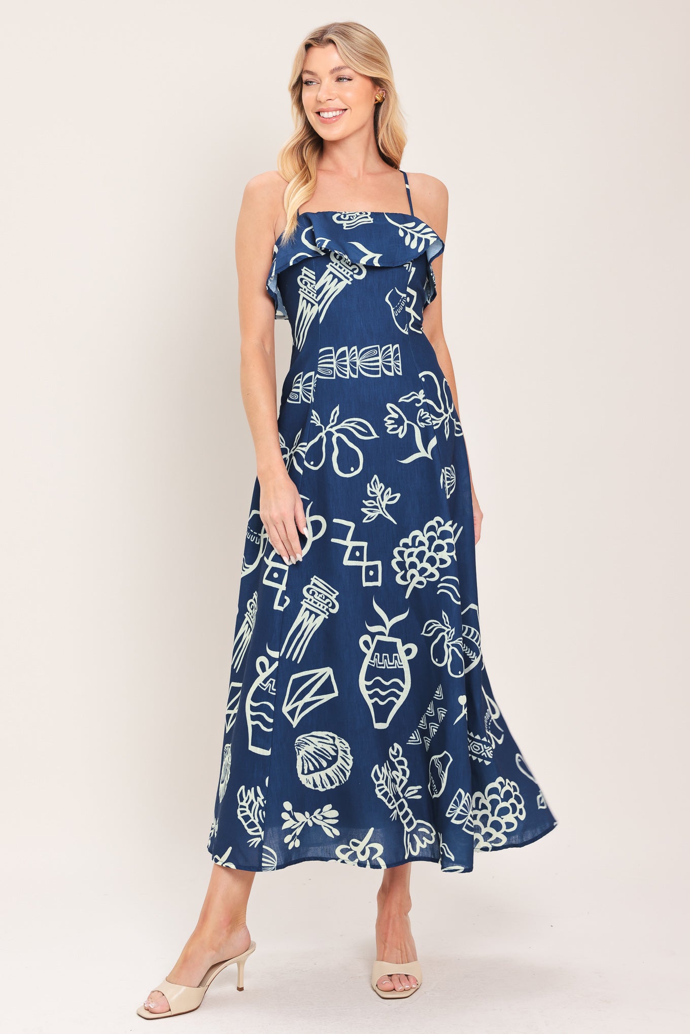 Woman wearing a navy blue midi dress with fruit and beach elements printed; featuring straight neckline with flounce, straps, circle skirt and back zipper closure | Flying Tomato