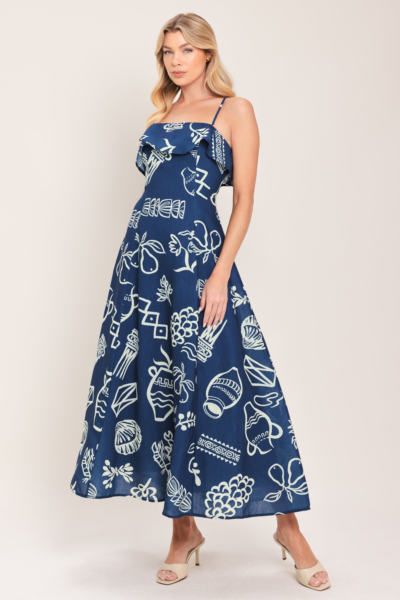 Woman wearing a navy blue midi dress with fruit and beach elements printed; featuring straight neckline with flounce, straps, circle skirt and back zipper closure | Flying Tomato