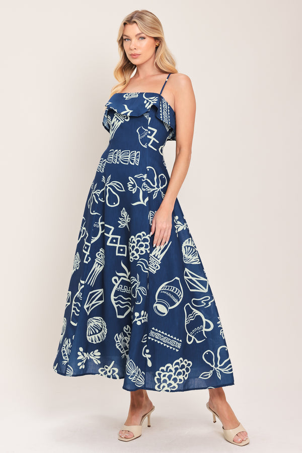 Woman wearing a navy blue midi dress with fruit and beach elements printed; featuring straight neckline with flounce, straps, circle skirt and back zipper closure | Flying Tomato