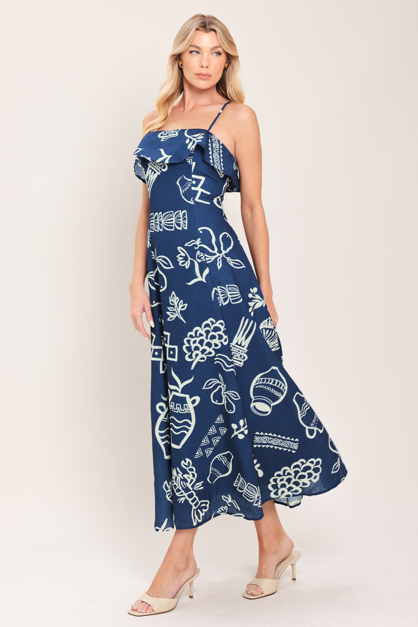 Woman wearing a navy blue midi dress with fruit and beach elements printed; featuring straight neckline with flounce, straps, circle skirt and back zipper closure | Flying Tomato