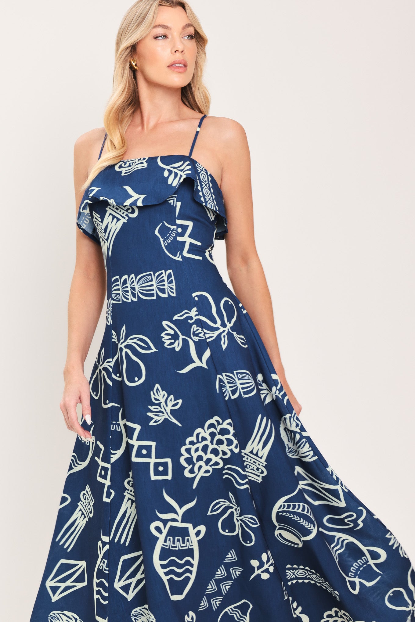 Woman wearing a navy blue midi dress with fruit and beach elements printed; featuring straight neckline with flounce, straps, circle skirt and back zipper closure | Flying Tomato