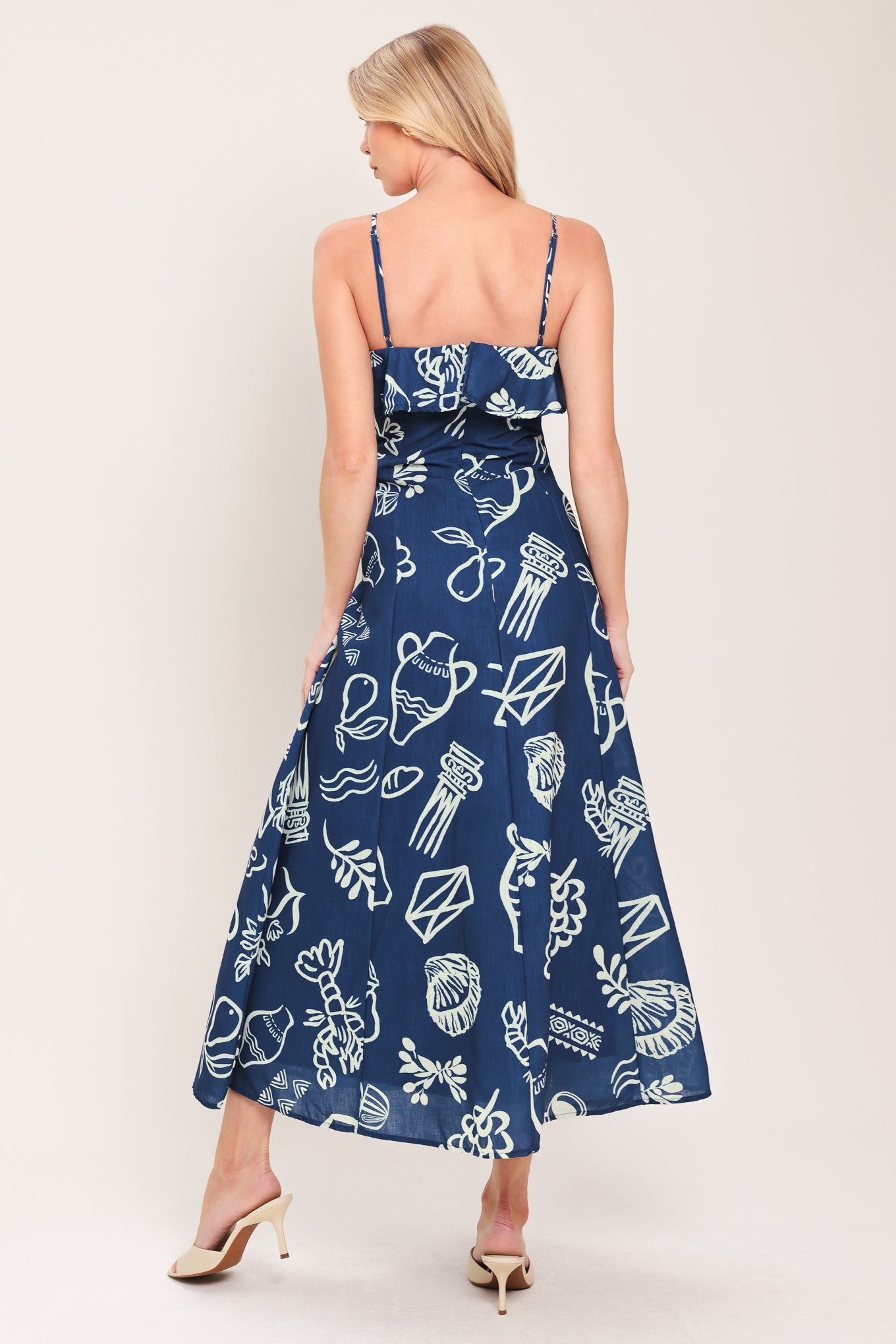 Woman wearing a navy blue midi dress with fruit and beach elements printed; featuring straight neckline with flounce, straps, circle skirt and back zipper closure | Flying Tomato
