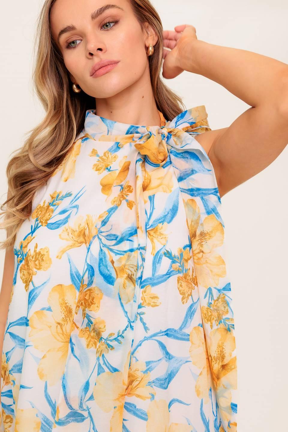 A printed woven mini dress featuring high neckline with bow tie, sleeveless, drop waist, ruffle hemline and back button closure.