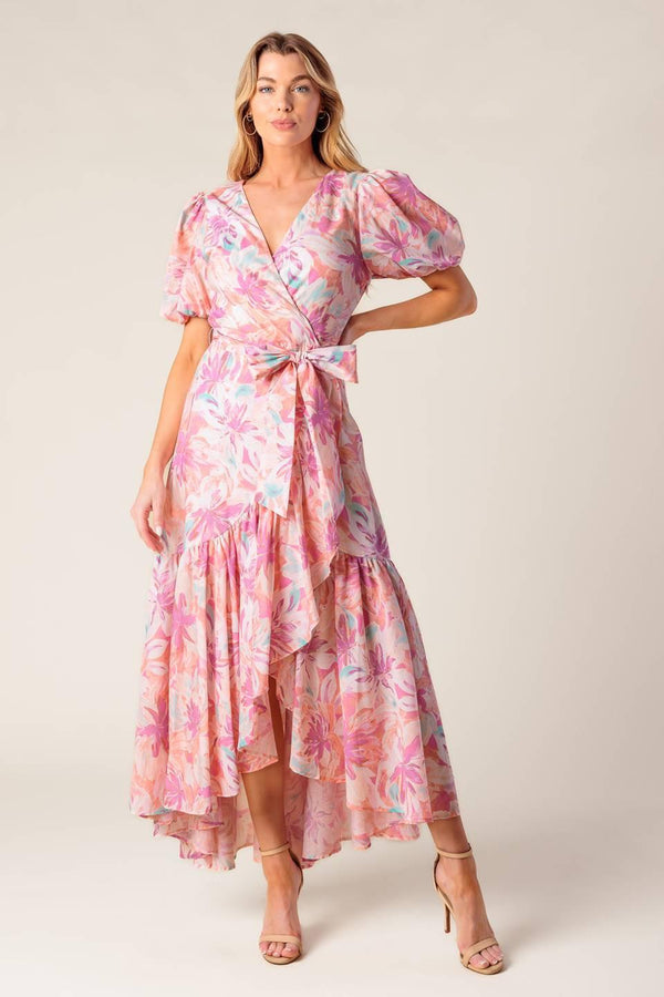 A printed woven hi-lo midi dress featuring surplice neckline, short puff sleeve, self sash tie and ruffled hemline