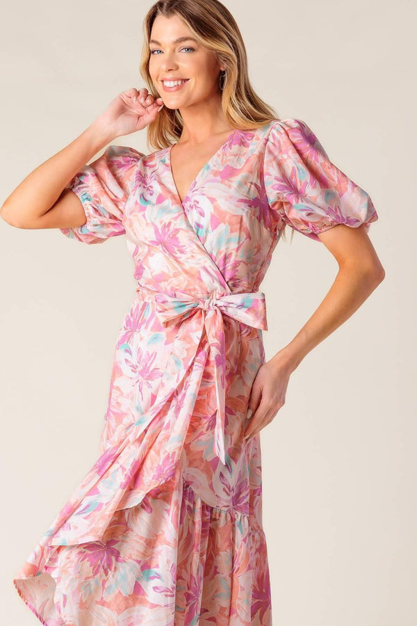 A printed woven hi-lo midi dress featuring surplice neckline, short puff sleeve, self sash tie and ruffled hemline