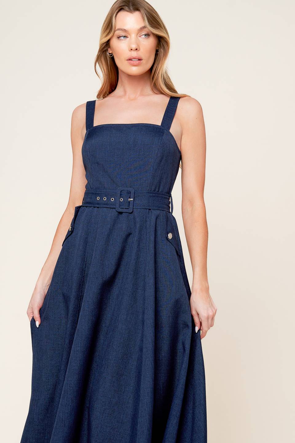 A solid woven midi dress featuring straight neckline, straps, self belt, side pockets, full skirt and back zipper closure