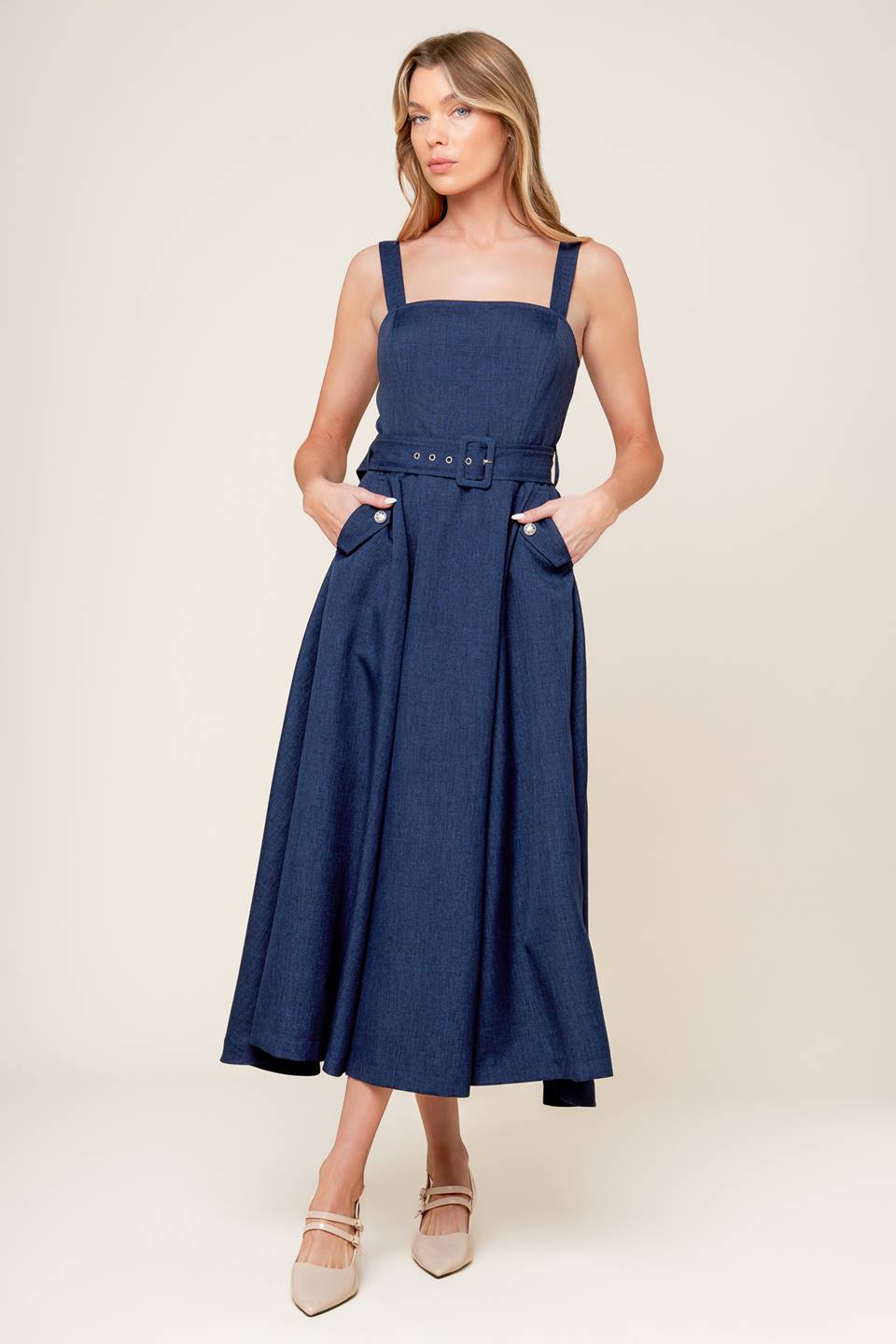 A solid woven midi dress featuring straight neckline, straps, self belt, side pockets, full skirt and back zipper closure