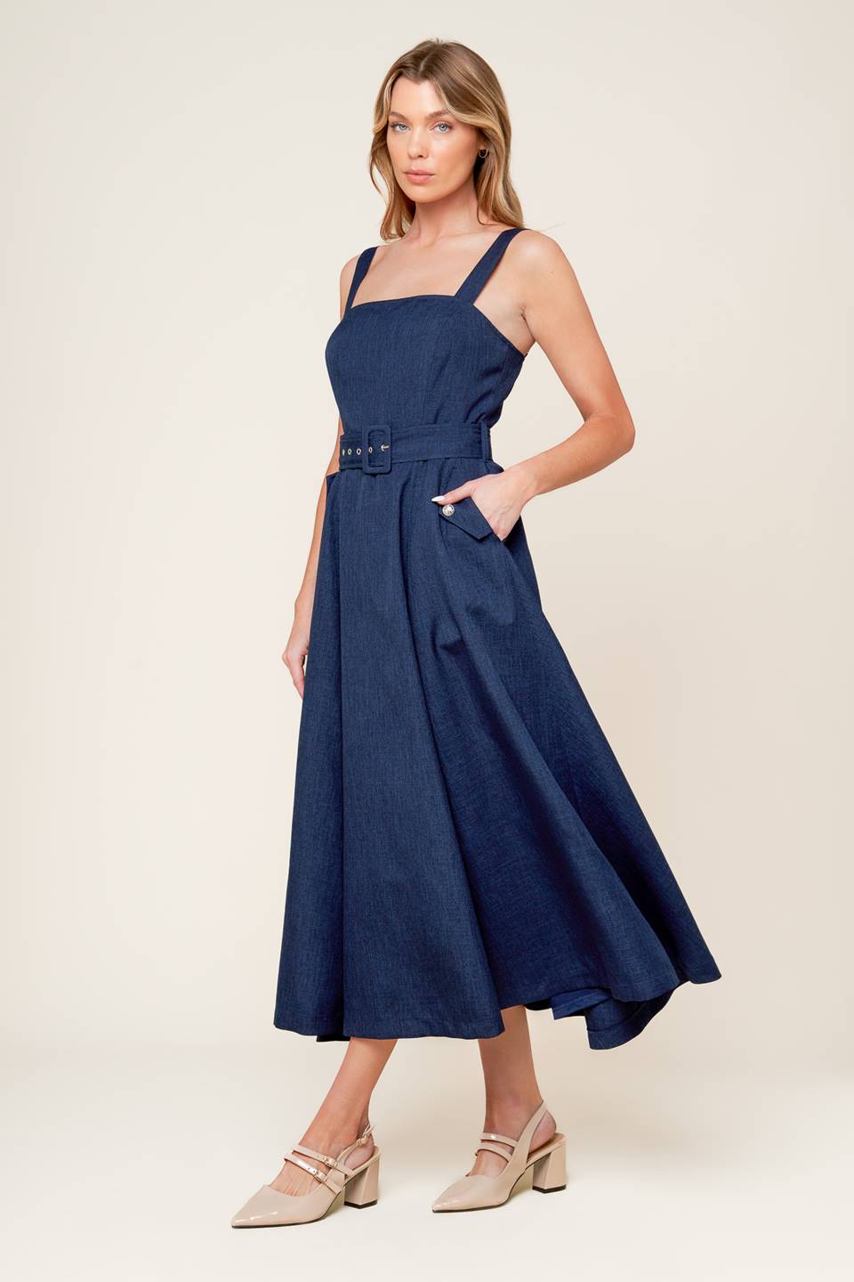 A solid woven midi dress featuring straight neckline, straps, self belt, side pockets, full skirt and back zipper closure