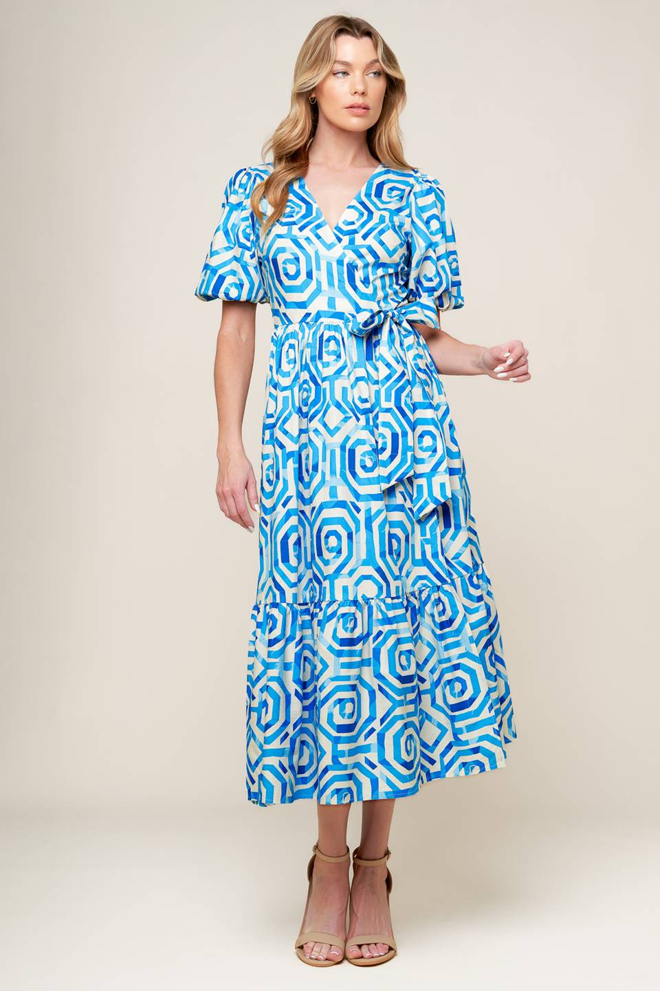 A printed blue and white woven midi dress featuring surplice neckline, short puff sleeve, true wrap with side tie and ruffled hemline.