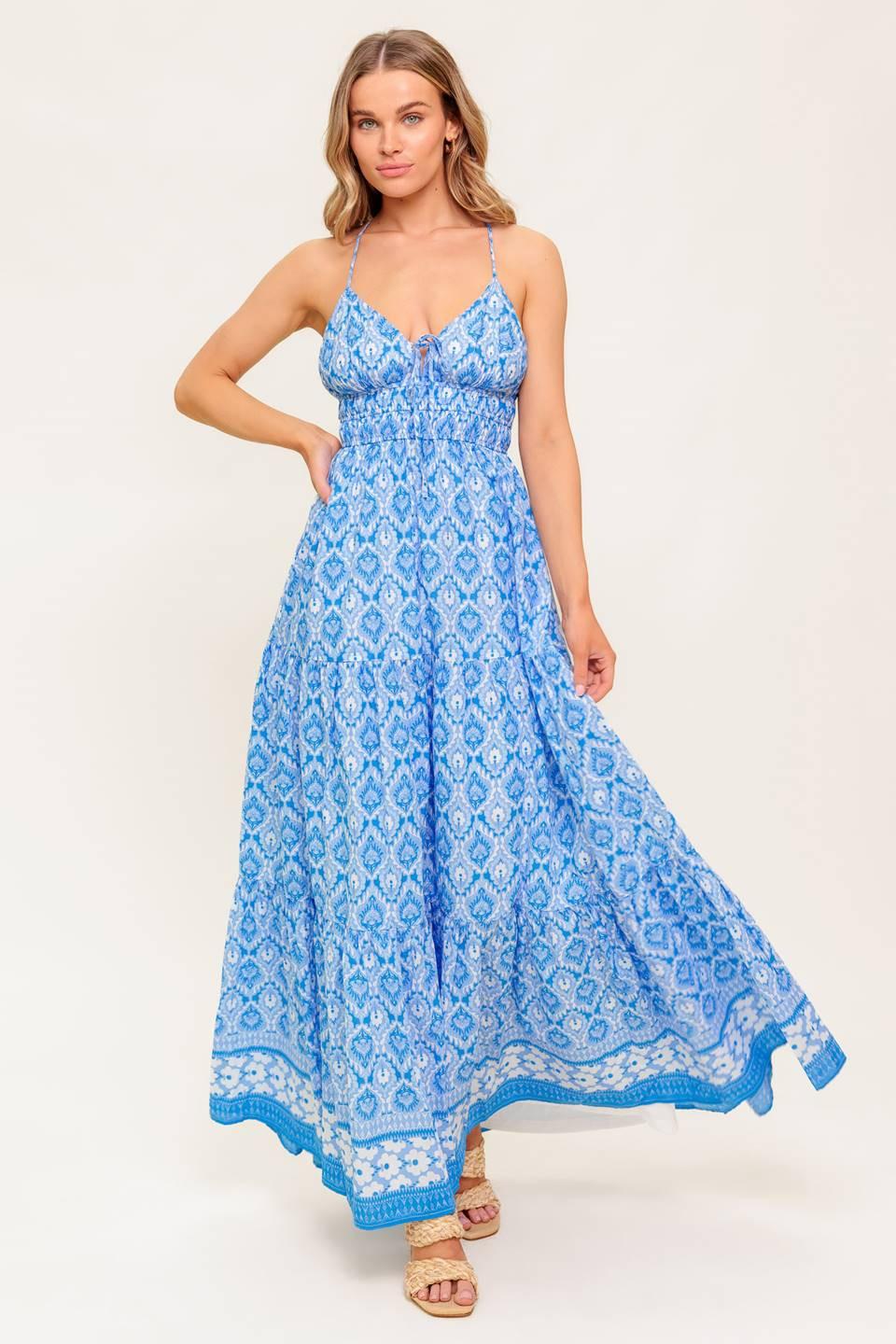 A printed woven maxi dress featuring cami top with center bow, smocked waist, tiered skirt and cross back strap.