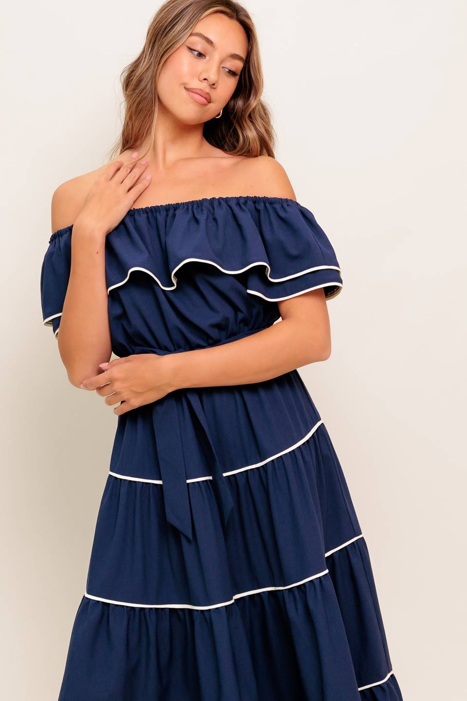 A solid navy woven midi dress featuring off shoulder neckline with flounce, elasticized waist, self sash tie and tiered skirt