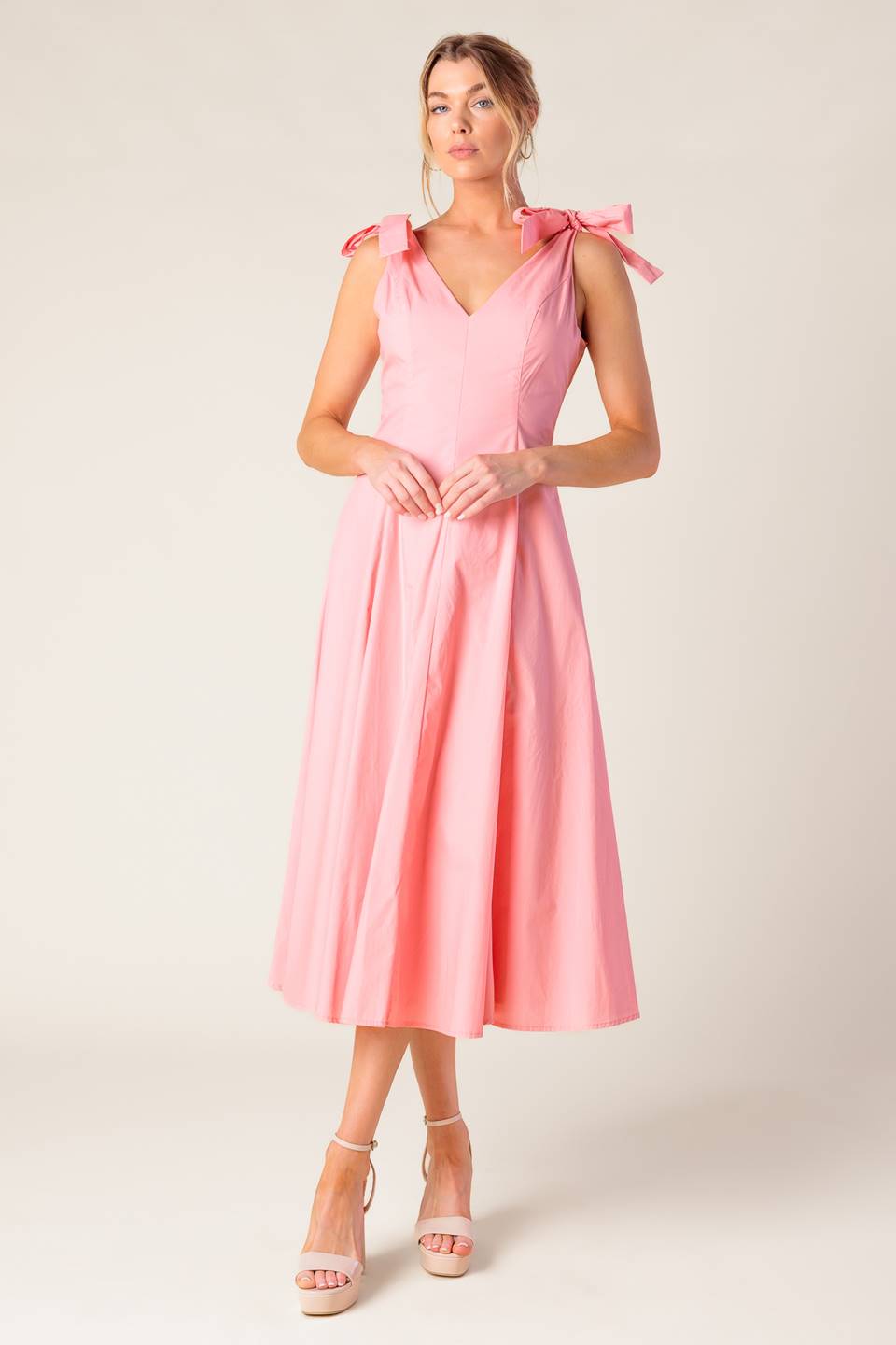 A solid light peach woven midi dress featuring front and back V neckline, shoulder bow detail, full skirt and back zipper closure