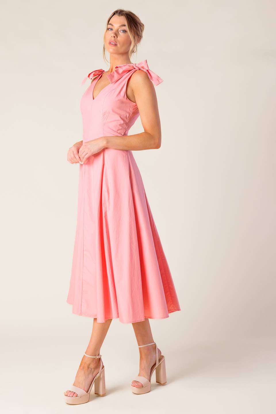 A solid light peach woven midi dress featuring front and back V neckline, shoulder bow detail, full skirt and back zipper closure