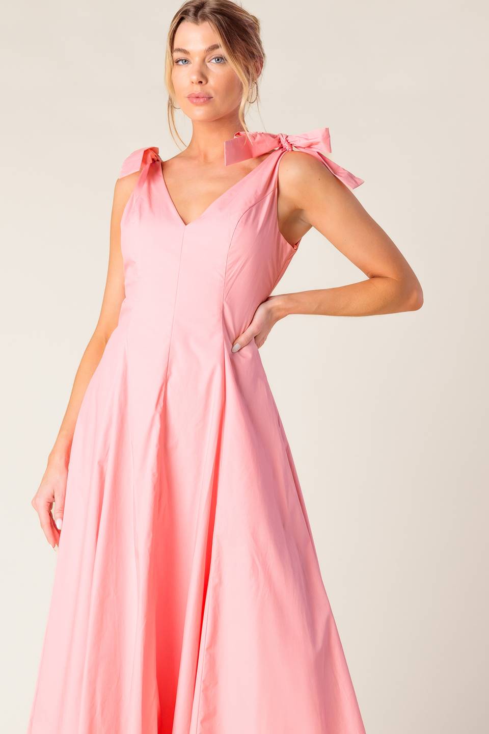 A solid light peach woven midi dress featuring front and back V neckline, shoulder bow detail, full skirt and back zipper closure