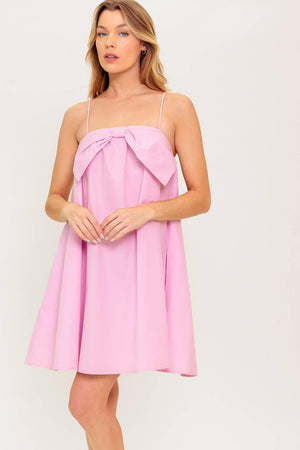 A pink solid woven mini dress featuring straight neckline, front bow detail and elasticized back