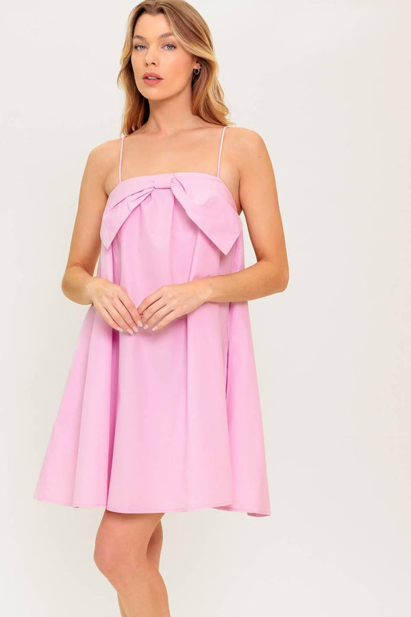 A pink solid woven mini dress featuring straight neckline, front bow detail and elasticized back