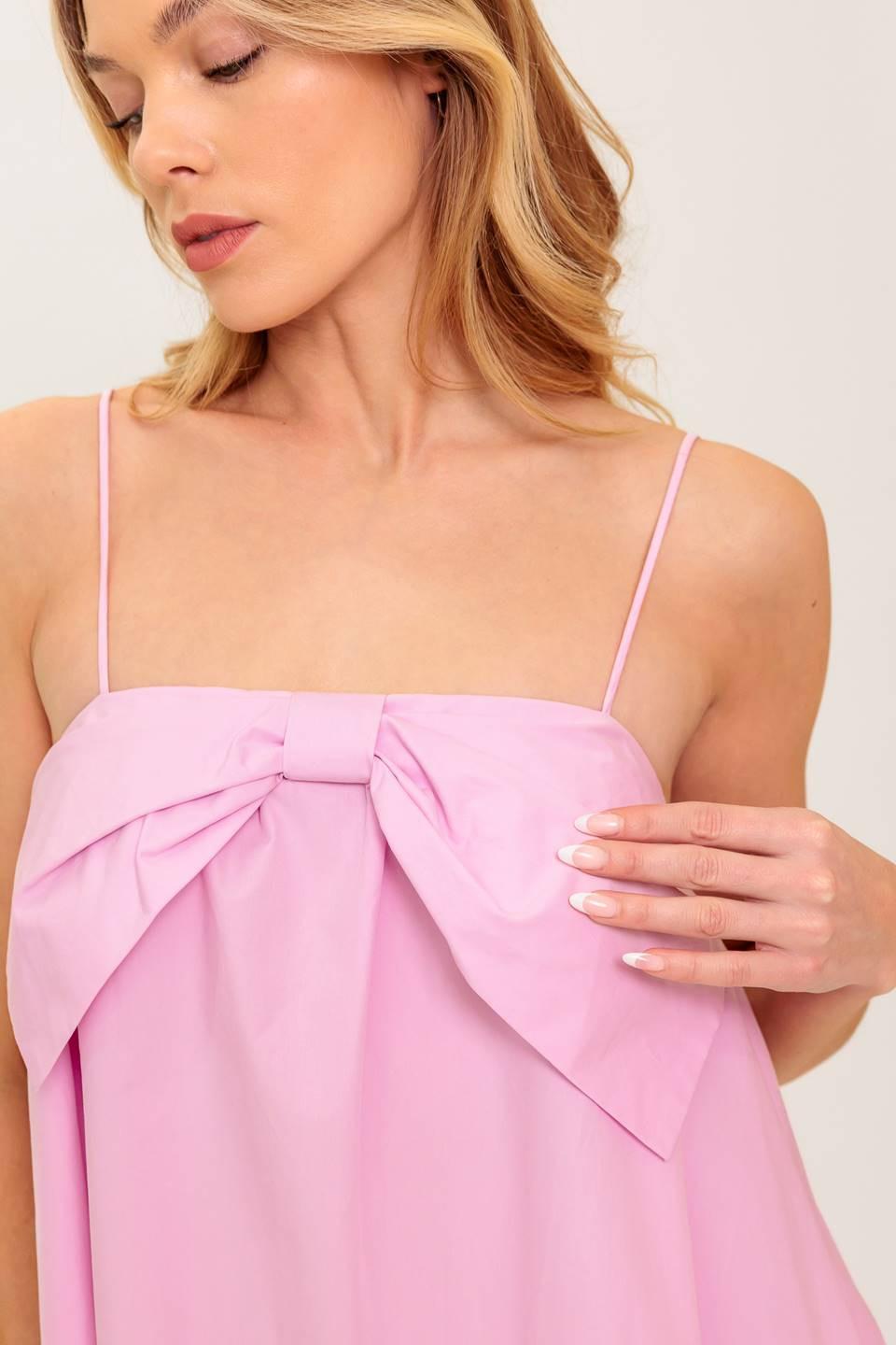 A pink solid woven mini dress featuring straight neckline, front bow detail and elasticized back