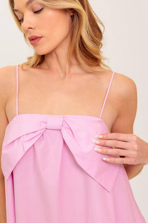 A pink solid woven mini dress featuring straight neckline, front bow detail and elasticized back
