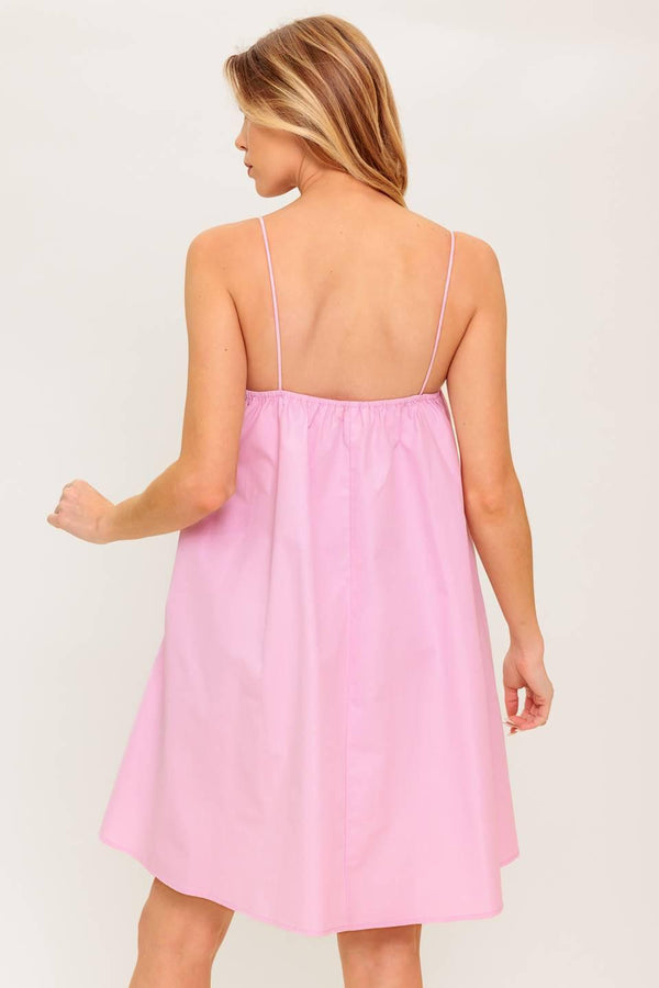 A pink solid woven mini dress featuring straight neckline, front bow detail and elasticized back