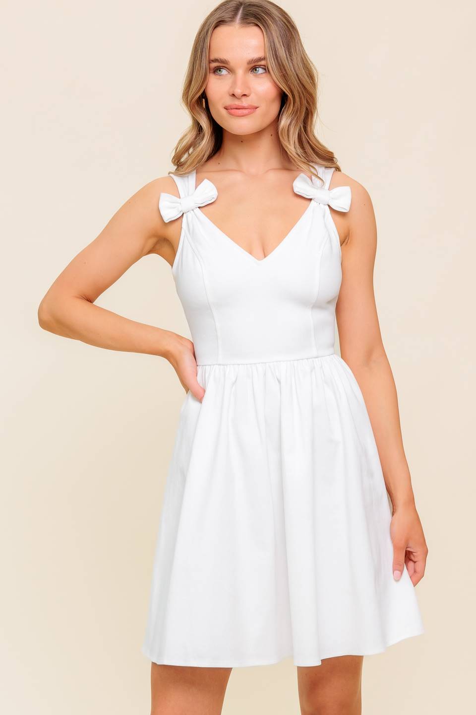 A solid white woven mini dress featuring V-neckline, straps with bow, full skirt and back zipper closure