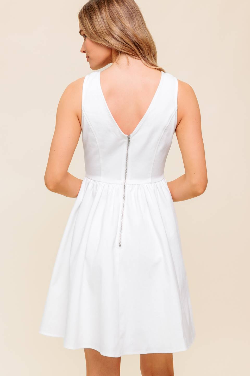 A solid white woven mini dress featuring V-neckline, straps with bow, full skirt and back zipper closure
