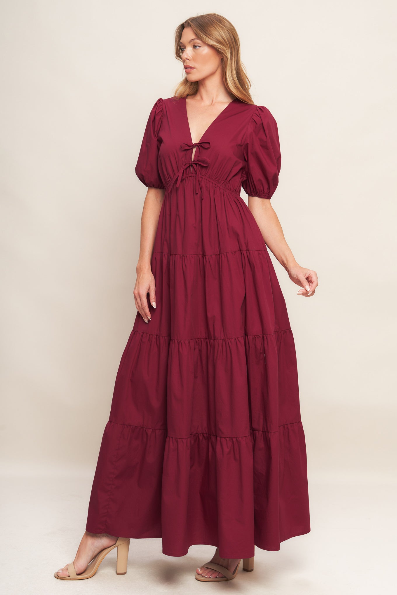 A solid woven maxi dress featuring V neckline with front bow closure, short puff sleeve, elasticized empire and tiered skirt.