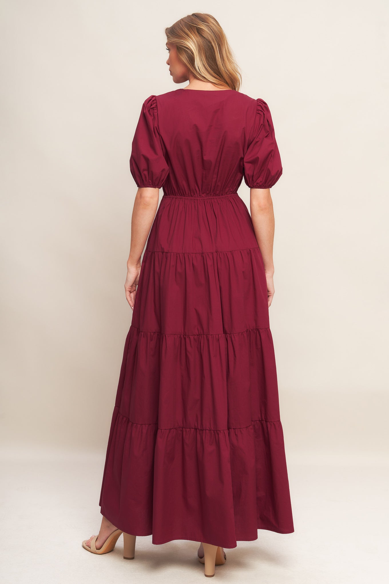 A solid woven maxi dress featuring V neckline with front bow closure, short puff sleeve, elasticized empire and tiered skirt.