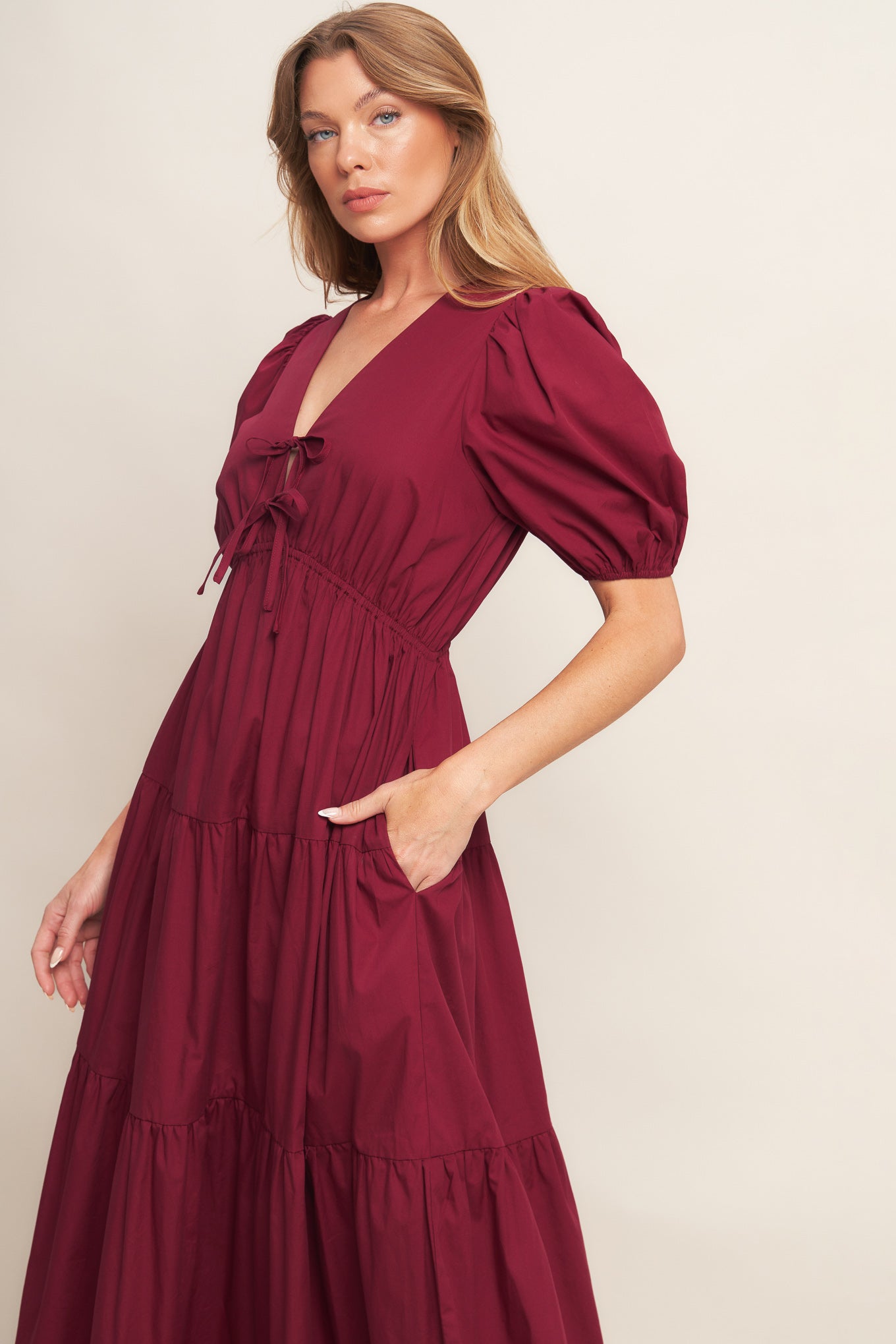 A solid woven maxi dress featuring V neckline with front bow closure, short puff sleeve, elasticized empire and tiered skirt.