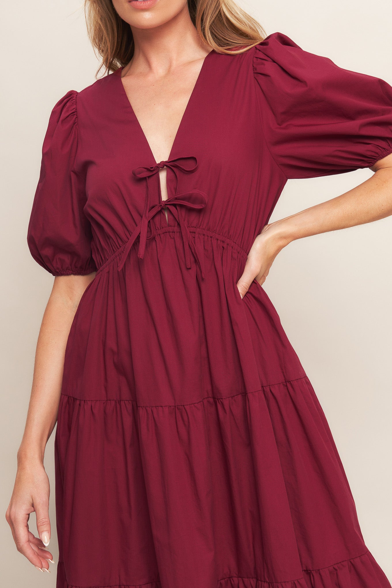 A solid woven maxi dress featuring V neckline with front bow closure, short puff sleeve, elasticized empire and tiered skirt.