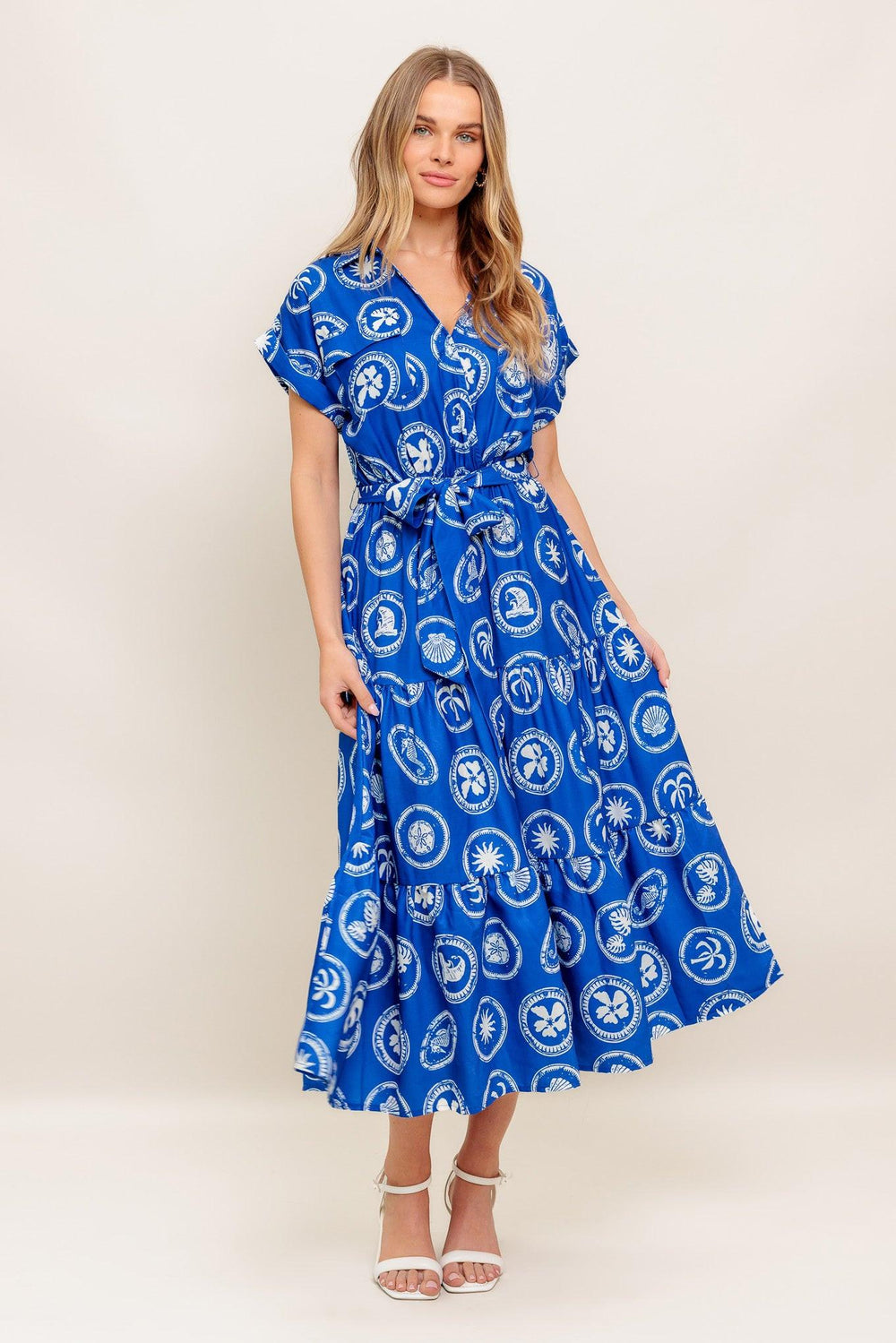A printed woven midi dress featuring collar, surplice bodice, short cuffed sleeve, elasticized waist, self sash and tiered skirt
