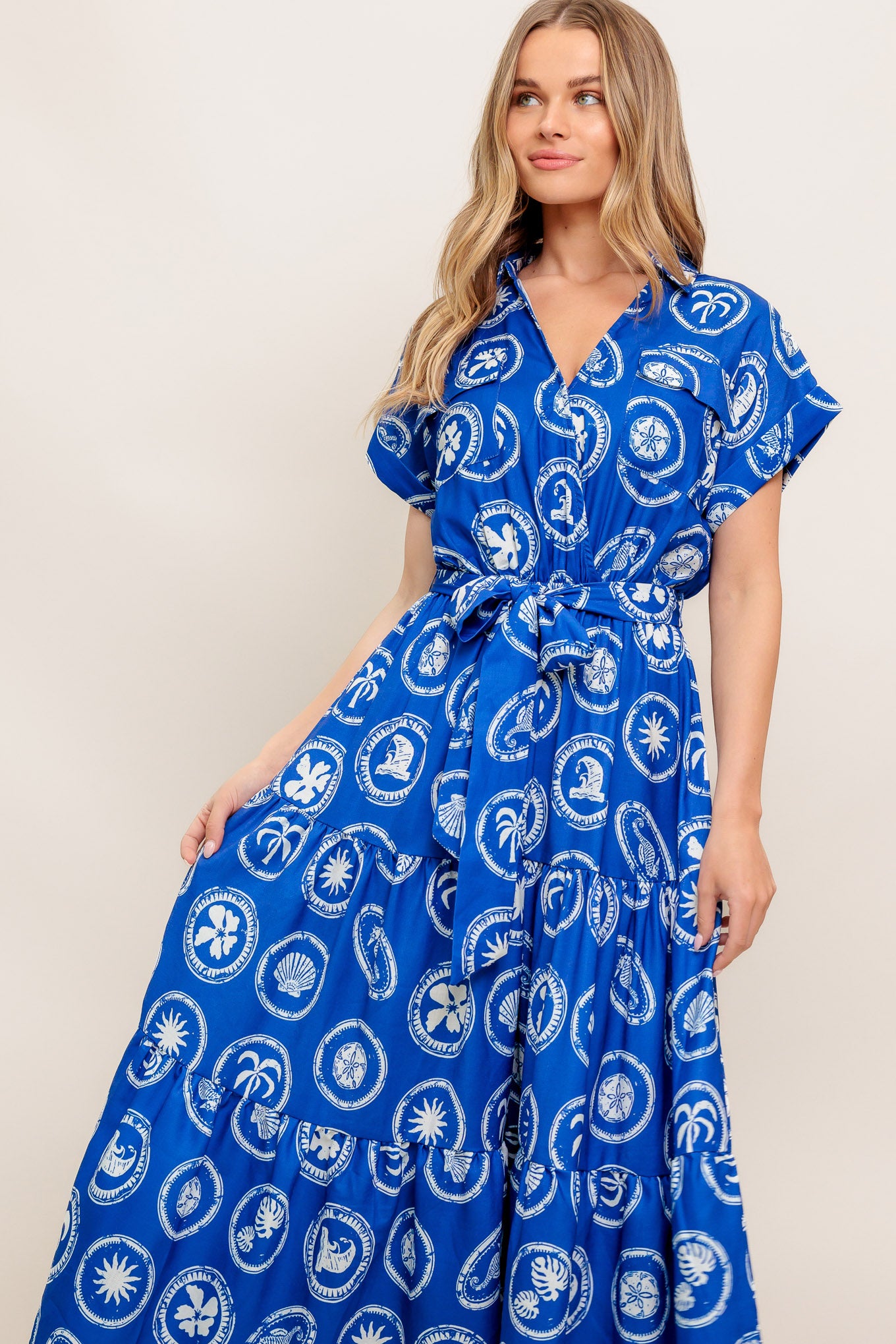 A printed woven midi dress featuring collar, surplice bodice, short cuffed sleeve, elasticized waist, self sash and tiered skirt