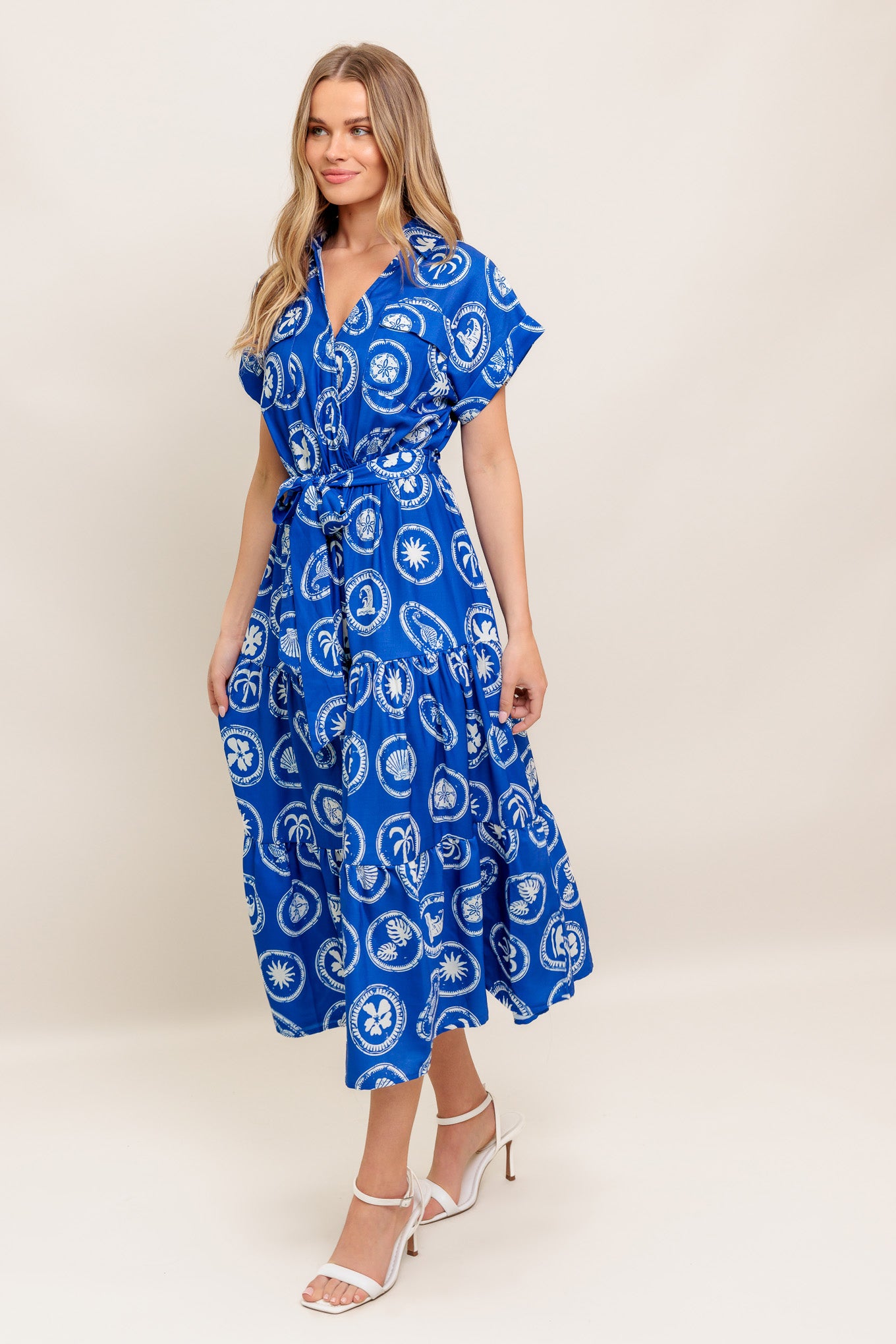 A printed woven midi dress featuring collar, surplice bodice, short cuffed sleeve, elasticized waist, self sash and tiered skirt